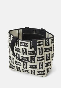 Sac fourre-tout tissé noir et blanc avec motif de texte répétitif "KARL LAGERFELD", anses noires et poche intérieure zippée visible.