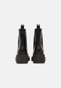 Czarne skórzane botki za kostkę z elastycznymi panelami po bokach, kwadratowymi noskami i masywną, czarną podeszwą na platformie. Widoczne pętelki do ściągania z tyłu.