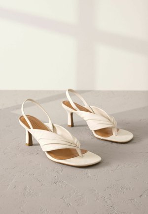Bela usnjena slingback čevlja z zvitjem spredaj, odprtim prstom in srednje višino blok peto. Gladka tekstura in minimalni detajli.
