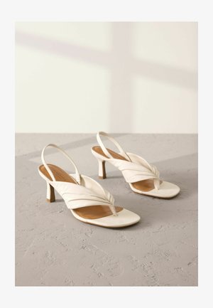 Talons slingback en cuir blanc avec un design avant torsadé, bout ouvert, et un talon bloc de hauteur moyenne. Texture lisse et accents minimaux.