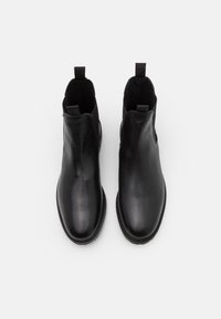 Las botas de cuero negro hasta el tobillo cuentan con una textura suave, puntera redondeada, paneles laterales elásticos y lengüetas de tirón para ponérselas fácilmente.