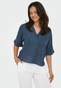 Camicia azzurra a maniche corte in tessuto leggero con bottoni frontali e colletto a intaglio, abbinata a pantaloni bianchi, morbidi e comodi.