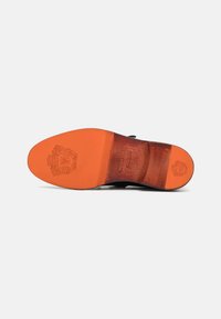 Sole de pantof negru din piele, cu un accent portocaliu vibrant, având un finisaj texturat și detaliu cu logo gravat. Formă plată, ușor curbată.