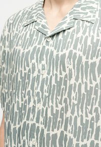 Πουκάμισο με κοντά μανίκια και κουμπιά, με αφηρημένο μοτίβο γκρι πινελιές σε λευκό ύφασμα και μικρό κεντημένο λογότυπο στο στήθος.