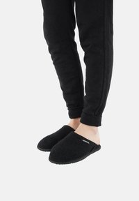 Czarne filcowe kapcie z otwartym noskiem i tyłem. Teksturowana cholewka z płaską gumową podeszwą i małą metką z logo z boku.