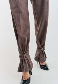 Hnedé na mieru šité nohavice s textúrovanou látkou; manžety previazané s klapkami a gombíkmi. Kombinované s čiernymi lodičkami na vysokom podpätku.