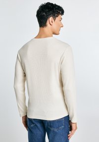 Langærmet, cremefarvet T-shirt med et struktureret strikkemønster og rund halsudskæring, kombineret med mørkeblå jeans.