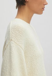Helles cremefarbenes Strickoberteil mit strukturiertem Finish, rundem Ausschnitt und überschnittenen Schultern, das eine lockere, entspannte Passform präsentiert.