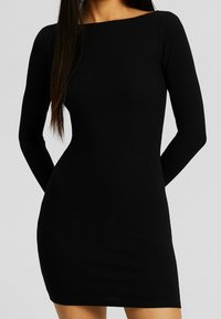 Robe noire à manches longues côtelées avec un col bateau, silhouette ajustée et texture lisse. Longueur au-dessus du genou avec un minimalisme dans les détails.
