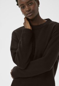 Dark brown knitted sweater with a ribbed round neckline and cuffs. Textured fabric with a relaxed fit, features slight drop shoulders.