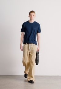 Σκούρο μπλε t-shirt με στρογγυλή λαιμόκοψη, μπεζ παντελόνια φαρδιάς γραμμής, μαύρη ζώνη και μαύρη τσάντα ώμου, με απαλές υφές και άνετη εφαρμογή.