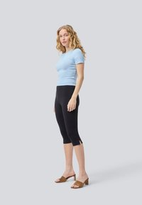 Light blue fitted ribbed t-shirt, black capri leggings with slits at the hem, and brown heeled mules. Simple, soft textures and contrasting colors.