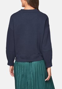 Marinblå sweatshirt med avslappnad passform, rund halsringning och sänkta axlar, tillsammans med en grön plisserad kjol.