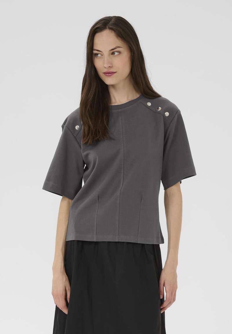 Tumehall lühikeste varrukatega särk siledast kangast, ümmarguse kaelusega, õmbluste detailide ja metallsete aksessuaaridega õlgadel.