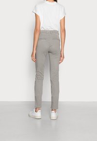 Pantalon gris slim en coton doux avec deux poches arrière et une texture lisse, associé à des baskets blanches et une chemise blanche à manches courtes.
