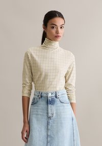 Lange mouw coltrui in crème met een ruitpatroon, gecombineerd met een lichtblauwe denim rok met een knoopsluiting aan de voorkant en zakken.