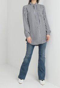 Svart- och vitrutigt skjorta med långa ärmar, knäppning framtill och en enda bröstficka, tillsammans med utvidgade blå jeans och vita skor.