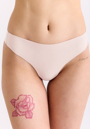 Taille und obere Oberschenkel einer Person, die nahtlose hautfarbene Unterwäsche trägt, mit einem Rosen-Tattoo am linken Oberschenkel und einem "FOREVER"-Tattoo an der rechten Hüfte.