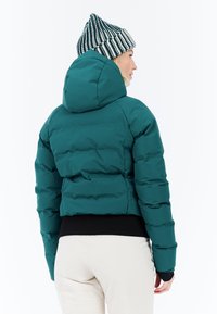 Mėlynas pūkinis džemperis su kapišonu, trumpas dizainas, juodas banguotas apatinis kraštas ir lygus paviršius. Modelis dėvi dryžuotą megztą skrybėlę.