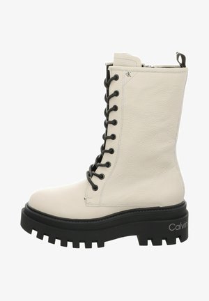 Stivale bianco in pelle con lacci e accenti neri, suola nera spessa, superficie texturizzata e logo sul lato esterno. Presenta una chiusura con zip.