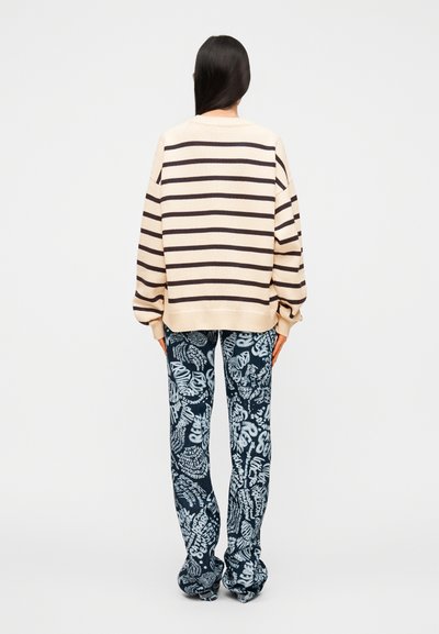 Pull beige à rayures bleu marine associé à un pantalon bleu à motifs avec un design graphique blanc, vu de dos.