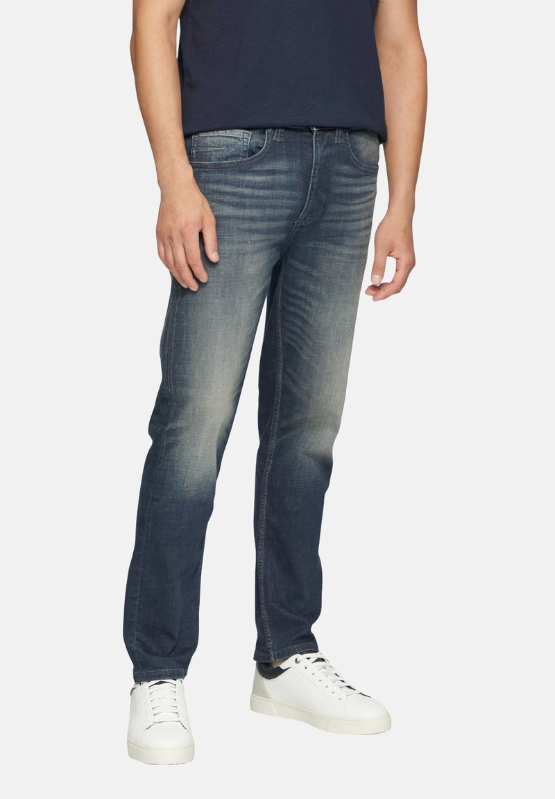 Jean en denim bleu foncé, coupe slim, léger délavage, cinq poches et fermeture à bouton. Associé à des baskets blanches et un t-shirt navy.