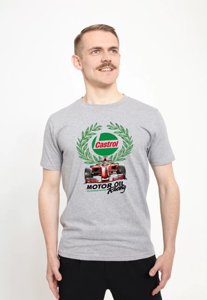 Mężczyzna w szarej koszulce z czerwonym samochodem Formuły 1, zielonym wieńcem laurowym i napisem „Castrol Motor Oil Racing” stojący na białym tle.