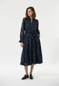 Dunkelblaues Spitzen-Midi-Kleid mit langen Ärmeln, einem Kragen und einem Gürtel. Blumenmuster auf dem gesamten Kleid, mit einem ausgestellten Rock und dekorativen Manschetten.