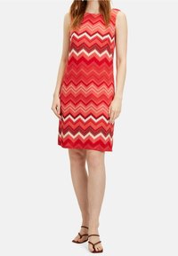 Czerwona bezrękawnik z wzorem w zygzak w różnych odcieniach czerwieni, różu i bieli. Gładki dzianinowy materiał o prostym kroju.