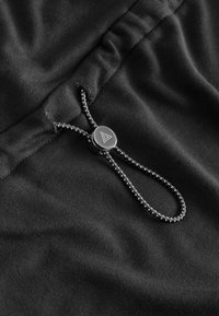Tissu noir avec une texture lisse, orné d'un anneau de tirage métallique avec un logo en triangle, attaché à un cordon de serrage.