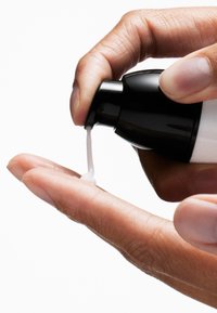 Bouteille en plastique noir et blanc pressant une fine crème blanche dans une main, mettant en valeur une texture lisse et un design de bouchon effilé.