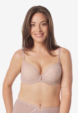 Uśmiechnięta kobieta z prostymi brązowymi włosami, ubrana w pasujący jasno-różowy koronkowy biustonosz i majtki na białym tle.