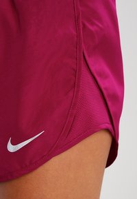Nike sportovní šortky v zářivém purpurovém odstínu, vyrobené z hladké tkaniny s perforovaným bočním panelem a malým reflexním logem.