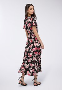 Abito maxi floreale con sfondo nero, motivi di fiori rosa e bianchi, maniche corte arricciate, dettaglio in vita, orlo fluido, abbinato a sandali bassi.