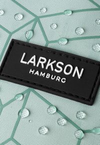 Tela verde texturizada con un patrón geométrico, que presenta una etiqueta rectangular negra que dice "LARKSON HAMBURG" en letras blancas, y gotas de agua.