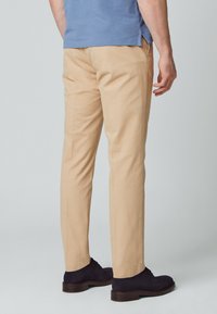 Beżowe, dopasowane spodnie wykonane z bawełny, charakteryzujące się gładką powierzchnią i delikatnym zwężeniem. Noszone z ciemnoniebieskimi zamszowymi butami.