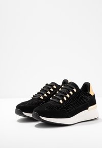 Svarta sneakers med överdel i mocka och mesh, med guldfärgade accenter, texturerade detaljer och en vit kilhälsåle.