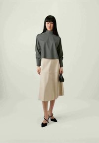 Skrajšani sivi pulover s turtleneck ovratnikom in dolgimi rokavi, v kombinaciji s bež midi krilom v A-liniji. Črne sandale s trakovi in majhna torbica.