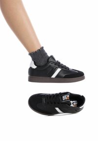 Zapatillas negras y blancas con una textura de cuero liso y ante, que presentan un diseño a rayas, parte delantera con cordones y suela de goma.