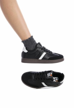 Zapatillas negras y blancas con una textura de cuero liso y ante, que presentan un diseño a rayas, parte delantera con cordones y suela de goma.