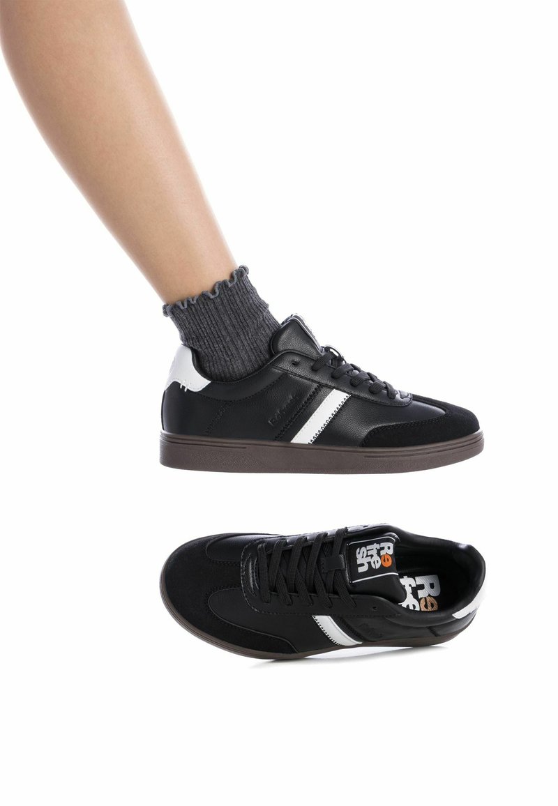 Zapatillas negras y blancas con una textura de cuero liso y ante, que presentan un diseño a rayas, parte delantera con cordones y suela de goma.