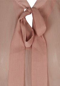 Blouse rose clair en tissu transparent, avec un col noué orné de liens drapés. Détails texturés et design doux et fluide.