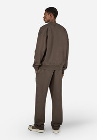 Brūns džemperis un atbilstošas bikses, izgatavotas no mīksta auduma. Brīva piegriezuma ar ribotiem piedurknēm. Vienkāršs dizains, bez rakstiem vai redzamām uzl�īmēm.