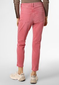 Jeans ajustados rosas con una cintura de media altura, bolsillos traseros y un dobladillo ligeramente recortado, combinados con zapatillas deportivas beige claras.