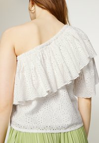 Top bianco off-shoulder con bordo in pizzo arricciato, caratterizzato da motivi floreali ricamati e una scollatura arricciata. Tessuto liscio e leggero.
