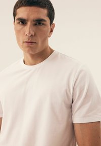 Biała bawełniana koszulka z okrągłym dekoltem i krótkimi rękawami, o gładkiej fakturze i klasycznym kroju, noszona przez modela.