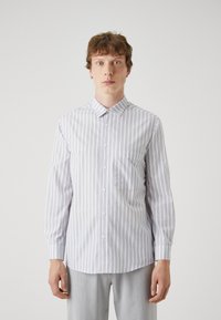 White shirt with vertical gray stripes, button-up design, pointed collar, long sleeves, and left chest pocket. Smooth texture, tailored fit.