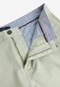 Pantalon pour homme vert clair avec braguette zippée, fermeture par bouton, et détails de ceinture intérieure rayée. Présente des accents de couture contrastants.
