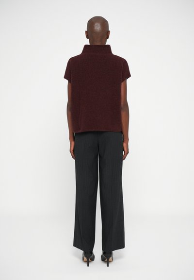 Top burdeos de manga corta con cuello alto, combinado con pantalones de pata de elefante a rayas negras y tacones stiletto negros. Diseño minimalista.