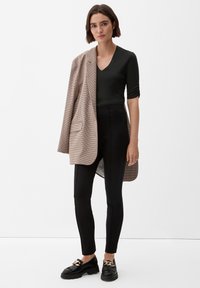 Zwarte, nauwsluitende broek, donkergroen V-hals top en een oversized beige geruite blazer. Chunky zwarte schoenen met gouden accenten. Soepele texturen door het geheel.